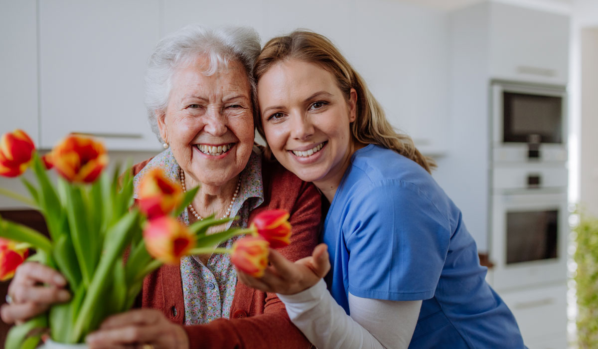 A caregiver and an elderly woman smiling together while holding a bouquet of tulips, representing compassionate in-home care by Mid-South Care Services in Memphis, TN.